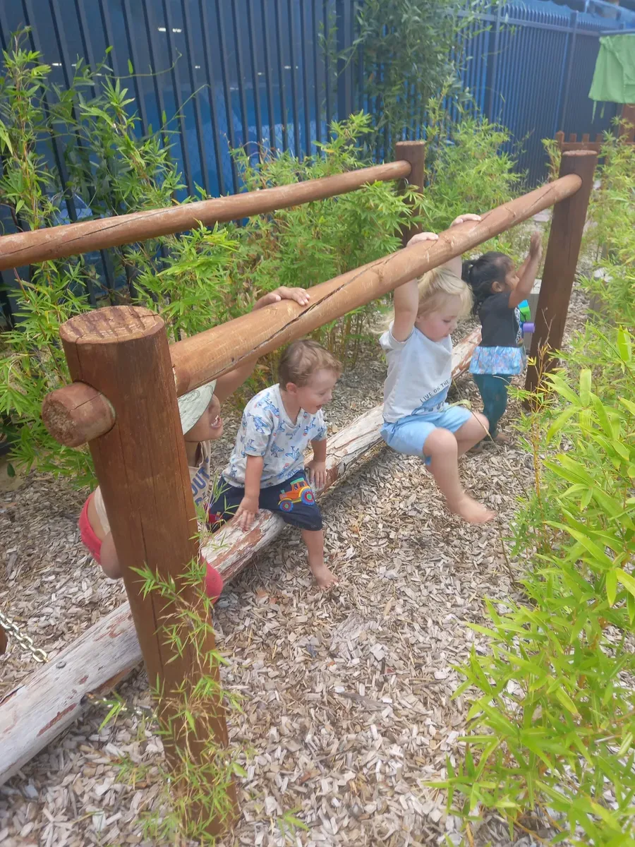 Children climbing and exploring in outdoor nature play area at Perth daycare