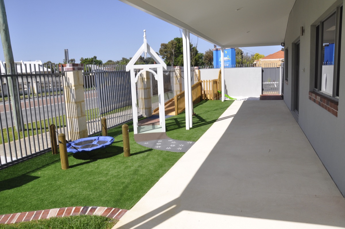 The outdoor play area at Sonas Woodbridge — synthetic grass, white pergola arch and a disc swing under the verandah