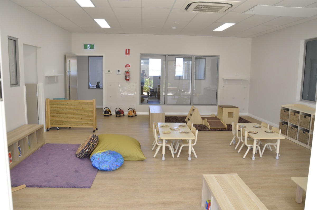 A toddler room at Sonas Woodbridge — natural-timber furniture, floor cushions and woven baskets of open-ended materials