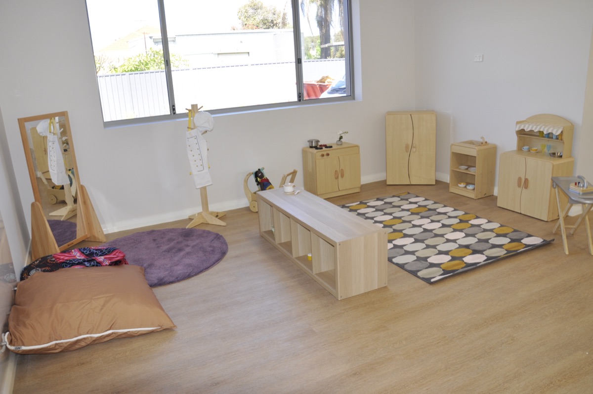 The home-corner studio at Sonas Woodbridge — wooden play kitchen, dress-ups including a chef coat, and a low mirror